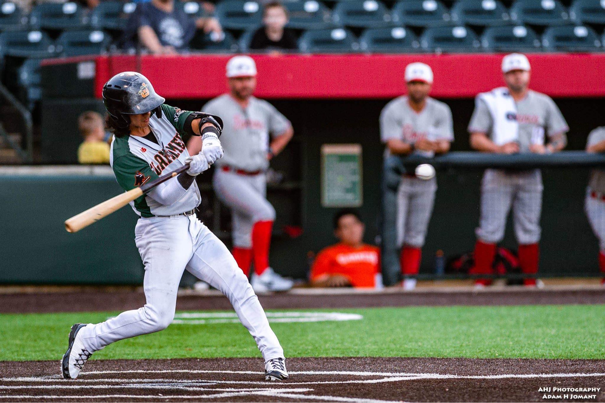Chaz Meadows in a full swing at bat during a professional game, dugout visible in background